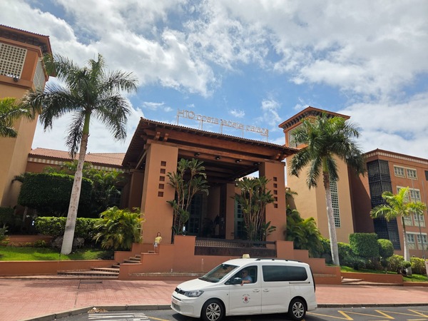 Entrada principal del hotel H10 Costa Adeje Palace con palmeras y fachada de estilo cálido en Tenerife.