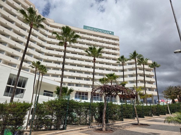 Edificio del hotel Iberostar en Costa Adeje visto desde la calle, con varias plantas, palmeras y nubes oscuras.