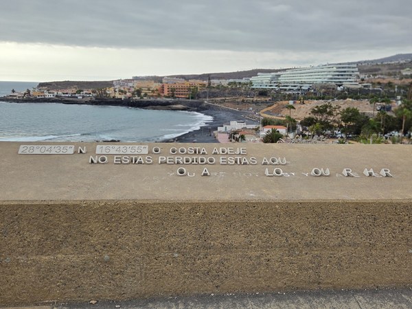 Mirador de Costa Adeje con la frase de ubicación grabada en un muro y vistas hacia la costa y varios hoteles.