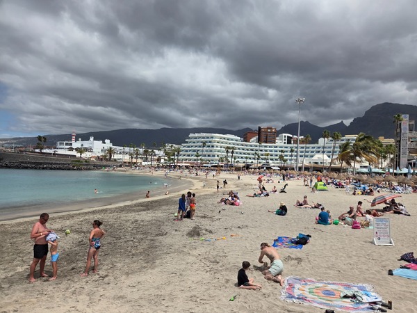 Playa de La Pinta Playa de La Pinta en Costa Adeje con arena clara, bañistas, hoteles y cielo cubierto.