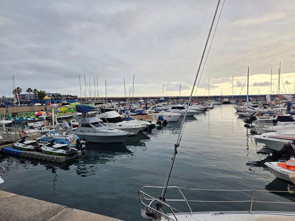 Puerto Colón con numerosas embarcaciones, motos de agua y el muelle bajo un cielo nublado al atardecer.