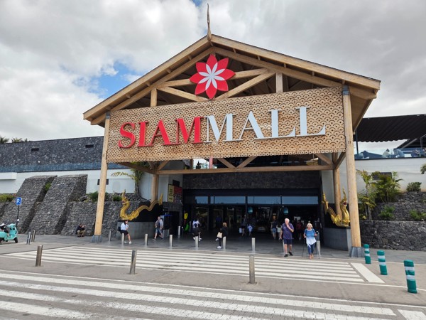 Entrada principal de Siam Mall con gran rótulo decorativo, estructura de madera y personas cruzando la calle.