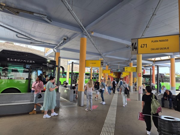 Interior de la estación de guaguas de Adeje con andenes numerados, viajeros esperando y autobuses de Titsa.